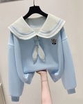 Light blue cropped sweatshirt with an ivory sailor collar striped in pale blue, an ivory tie and a crest, held up on a hanger