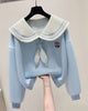 Light blue cropped sweatshirt with an ivory sailor collar striped in pale blue, an ivory tie and a crest, held up on a hanger