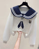 White cropped sweatshirt with a navy sailor collar striped in white, a navy tie and a crest, held up on a hanger