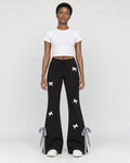Woman in black flared sweatpants with small white bows, a white cropped tee and white sneakers, full length