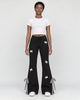 Woman in black flared sweatpants with small white bows, a white cropped tee and white sneakers, full length