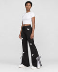 Woman in black flared sweatpants with white bows, turned slightly, with a tied gingham ribbon at the hem