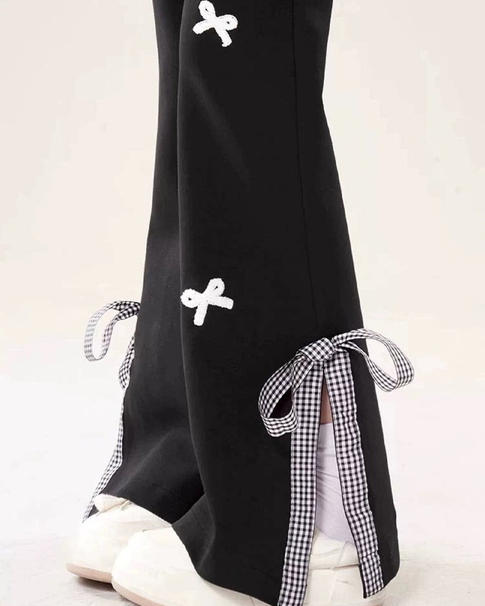Black flared sweatpants with a white bow on the thigh and a gingham ribbon tied at the slit hem