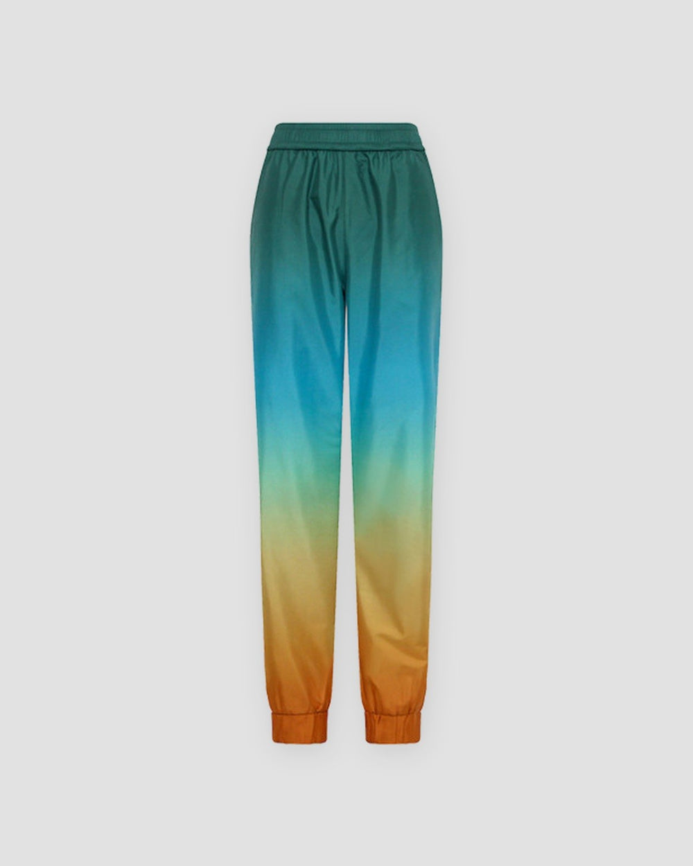 Gradient jogger pants laid flat, dark teal at the waist fading through cream to orange at the elastic cuffs