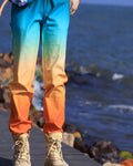 Gradient jogger pants fading from turquoise at the hips to cream at the knees and orange at the ankle cuffs, worn standing