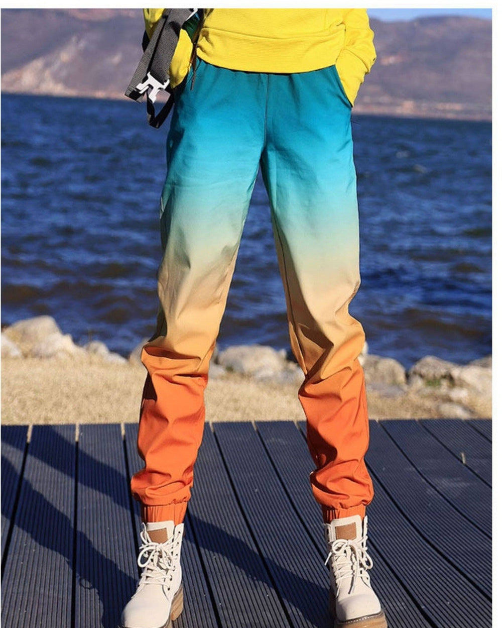 Woman standing in the gradient jogger pants with a yellow top, the fade from teal to orange at the cuffs