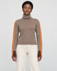 Woman standing in the herringbone turtleneck with orange sleeve stripes and cream trousers, front view