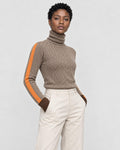 Woman in a brown herringbone turtleneck with an orange sleeve stripe and cream trousers, three-quarter view