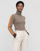 Woman in a brown herringbone turtleneck with an orange sleeve stripe and cream trousers, three-quarter view