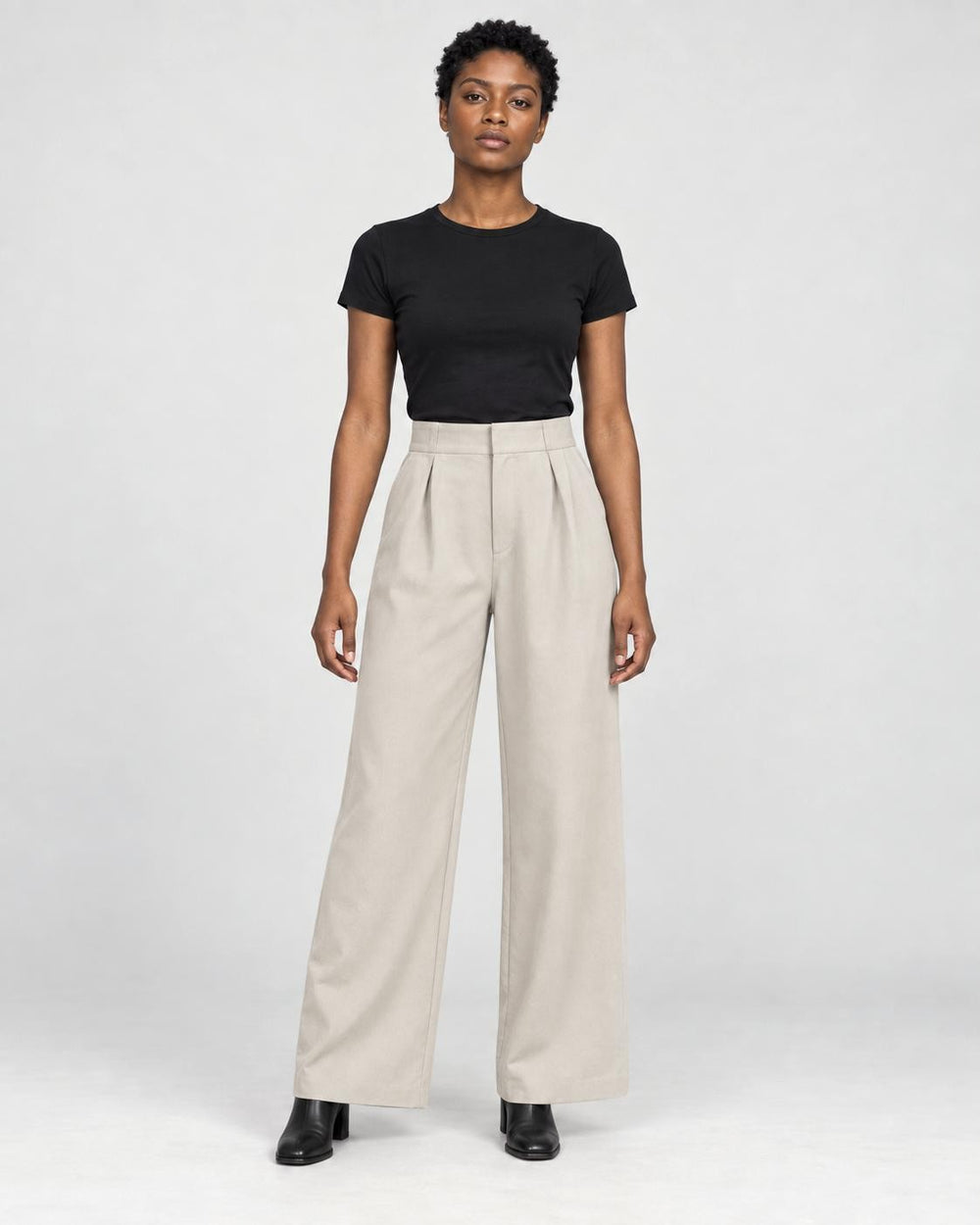 Model wearing the beige high-rise pleated wide-leg pants with a black tee and black boots, front view