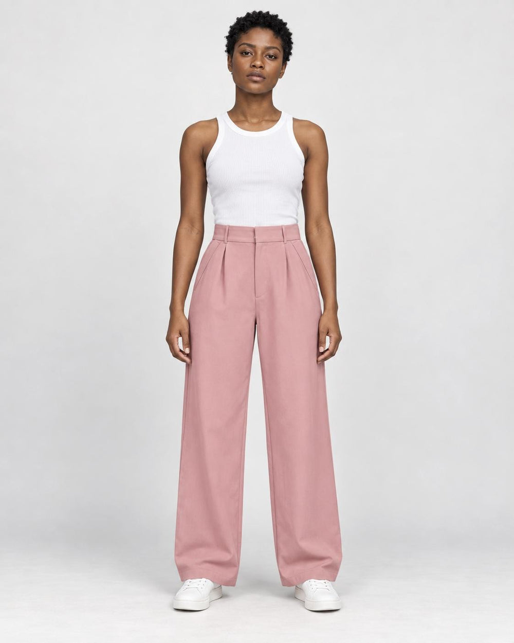 Model wearing the pink high-rise pleated wide-leg pants with a white tank top and white sneakers, front view