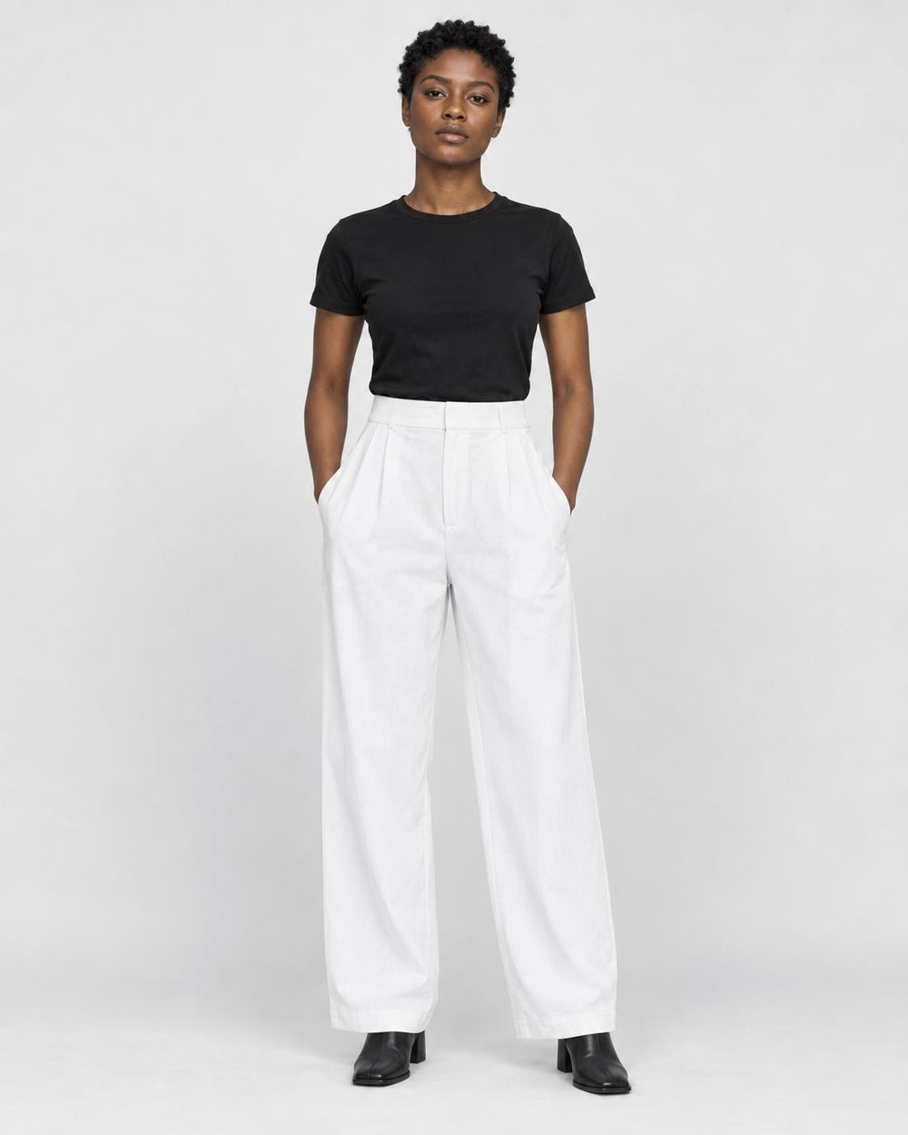 Model wearing the white high-rise pleated wide-leg pants with a black tee and black boots, front view