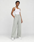 Model wearing the sage green high-rise pleated wide-leg pants with a white tank top and white sneakers, three-quarter view