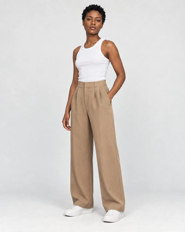 Model wearing the tan high-rise pleated wide-leg pants with a white tank top and white sneakers, three-quarter view