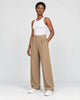 Model wearing the tan high-rise pleated wide-leg pants with a white tank top and white sneakers, three-quarter view