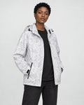 Model wearing the white leaf-print hooded windbreaker open over a black tee and black jeans, three-quarter view
