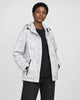 Model wearing the white leaf-print hooded windbreaker open over a black tee and black jeans, three-quarter view