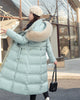 Mint long puffer coat with a khaki fluffy hood trim and a belt, worn with a small black shoulder bag