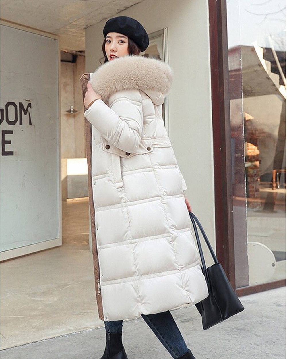 White long puffer coat with a khaki fluffy hood trim, a belt and wide channel quilting, worn with a black bag