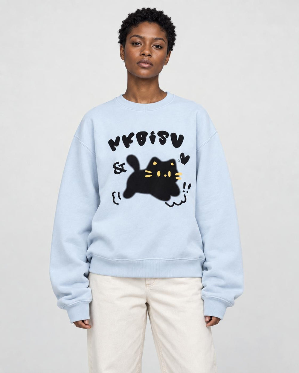 Woman in a light blue loose sweatshirt with a black cat print, cream trousers and white sneakers