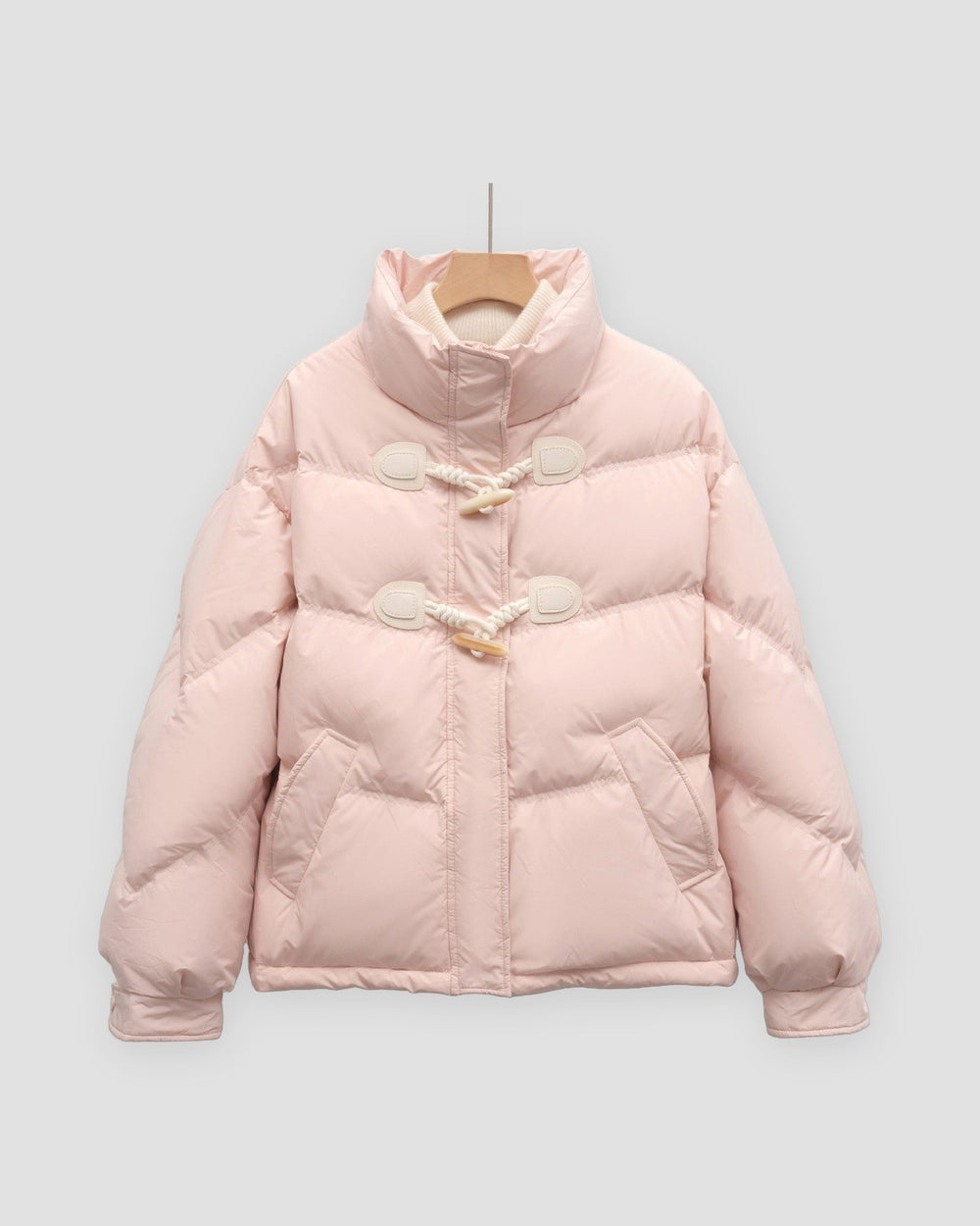 Pink short puffer jacket with chevron quilting, a stand collar and two horn toggles on cord loops, on a hanger