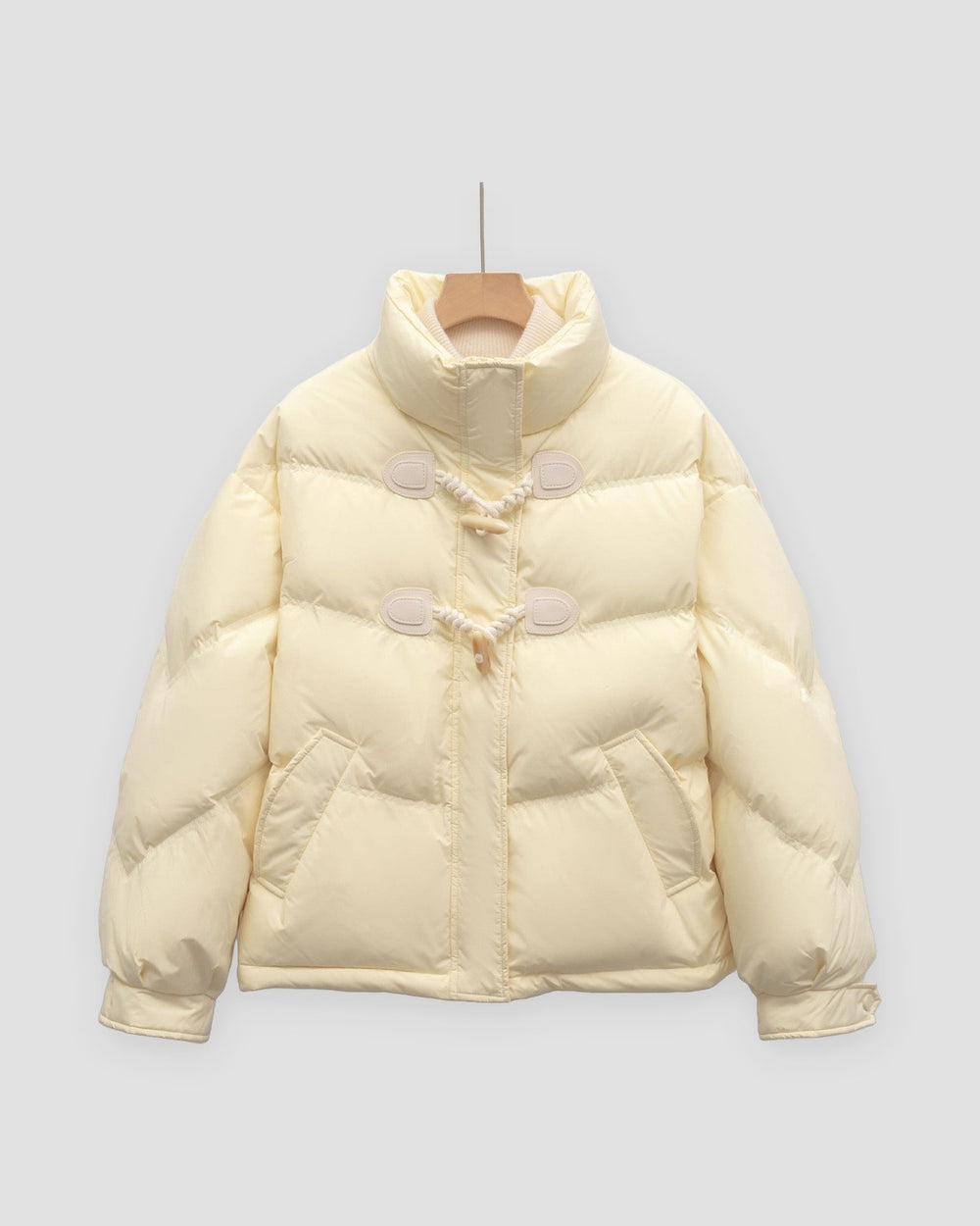 Pale yellow short puffer jacket with chevron quilting and two horn toggles on cord loops, on a hanger
