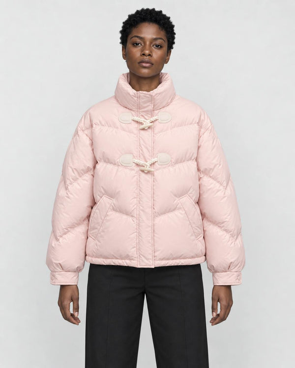Woman in a short pink puffer jacket with horn toggles over a black top and black trousers, torso to mid-thigh