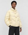 Woman in a pale butter-yellow short puffer jacket with horn toggles over a black top, turned slightly