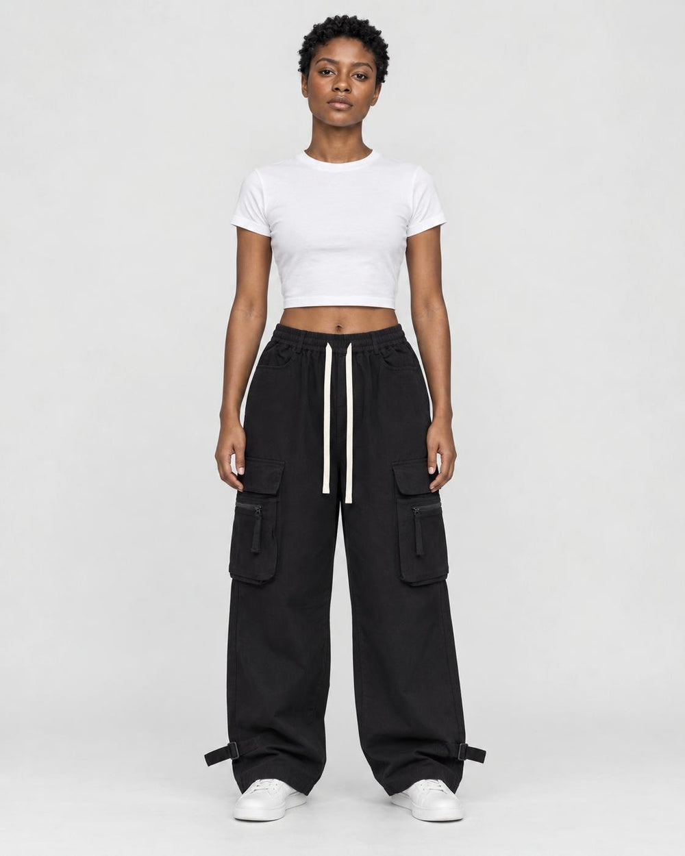 Woman in black wide-leg cargo pants with flap pockets, a white cropped tee and white sneakers, full length