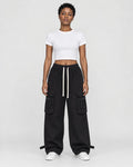 Woman in black wide-leg cargo pants with flap pockets, a white cropped tee and white sneakers, full length