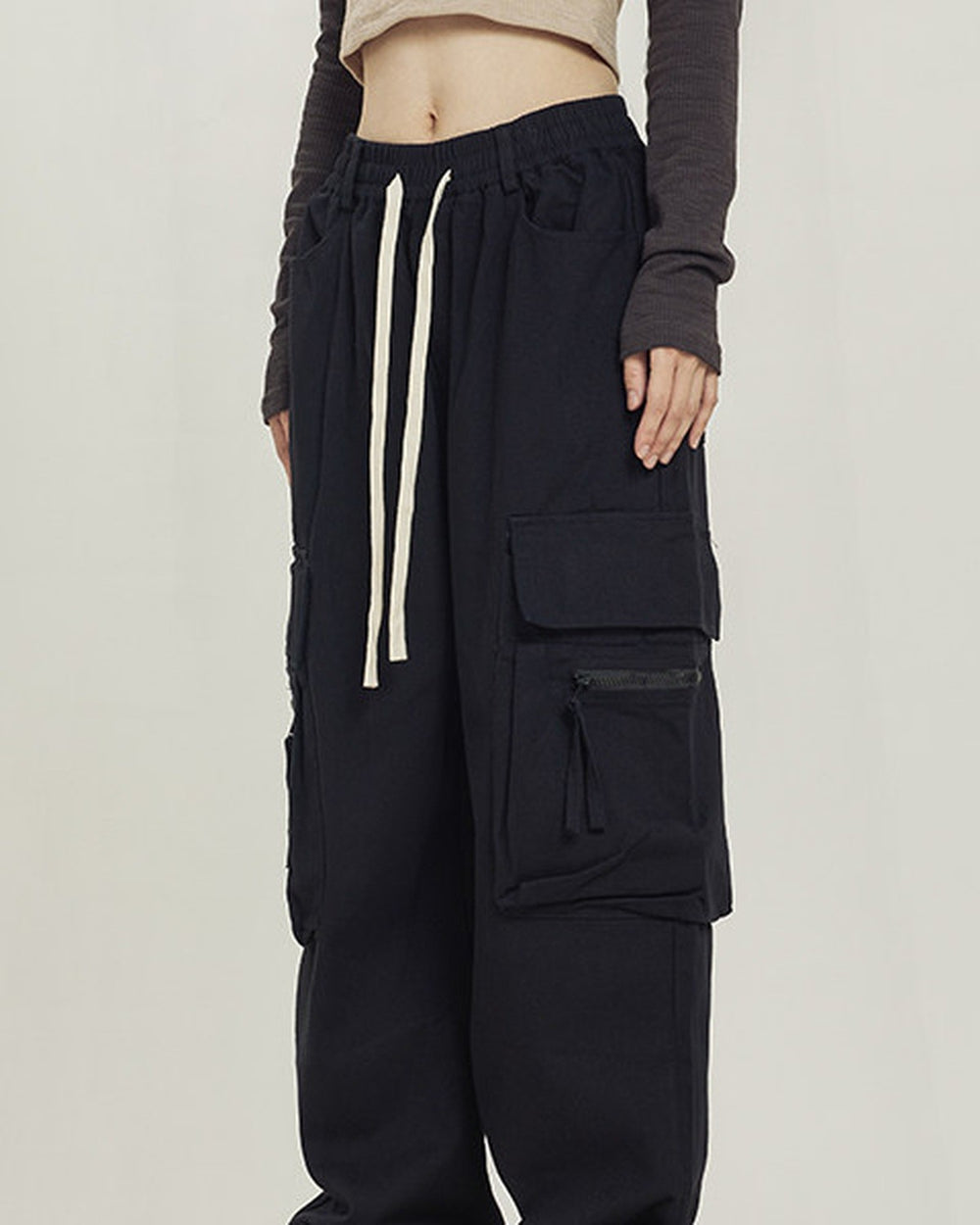 Black wide-leg cargo pants with big thigh pockets and a cream drawcord, worn standing
