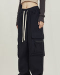 Black wide-leg cargo pants with big thigh pockets and a cream drawcord, worn standing